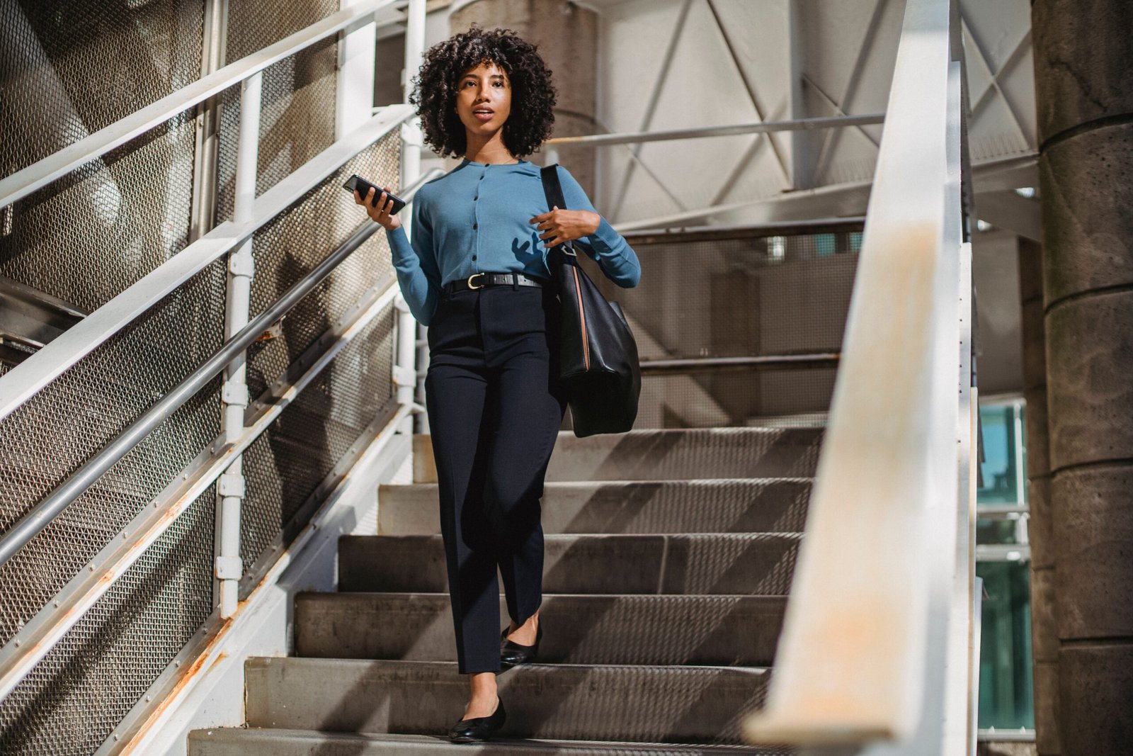 African American woman walking down stairs holding smartphone and bag.